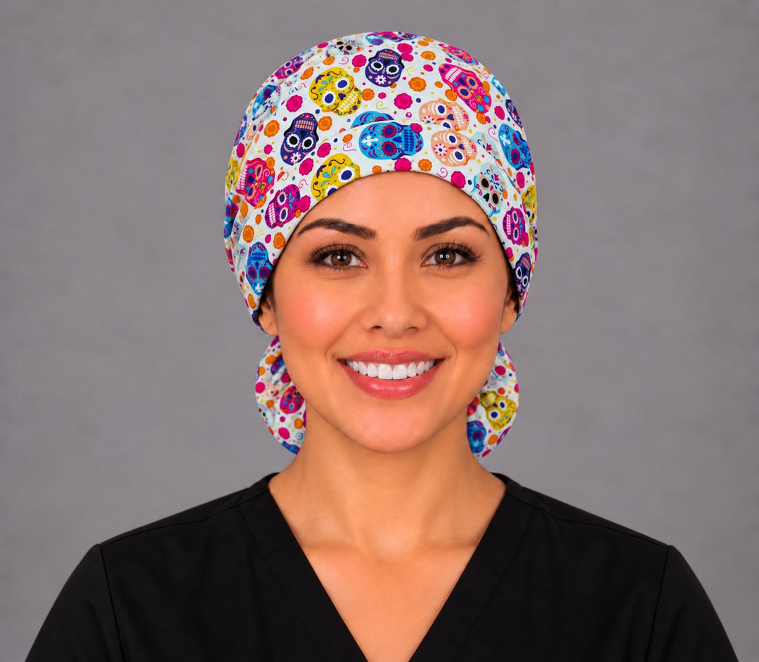 Smiling nurse in black scrubs wearing a cream sugar skull ponytail scrub cap, front view of the calavera print band with the pouch peeking out below