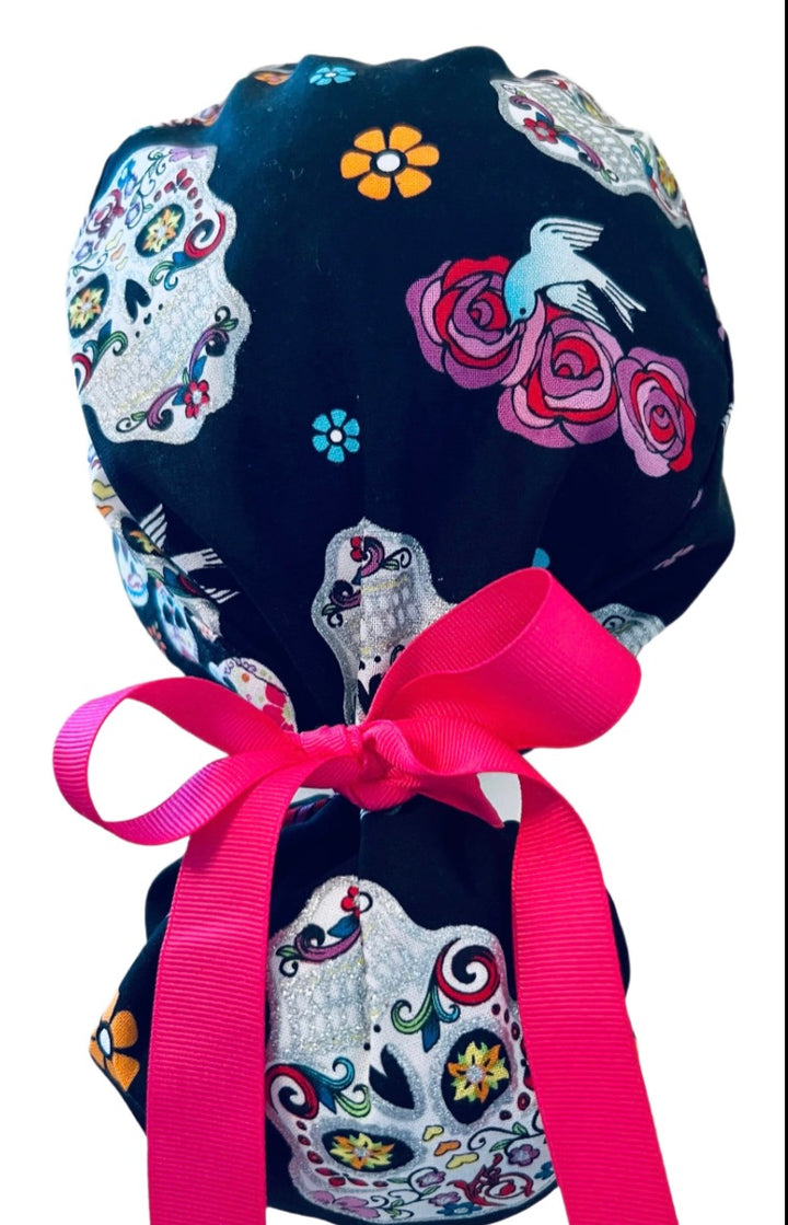 Sugar skull ponytail scrub cap back close-up showing gathered pouch of silver Day of the Dead skulls, roses and a bird on black with hot pink grosgrain ribbon bow