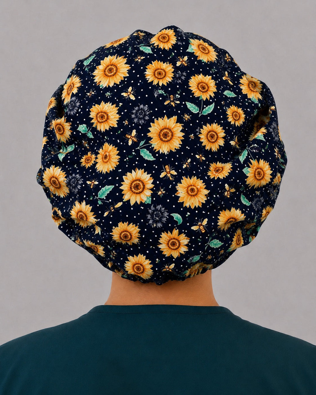 Back view of the sunflower bee bouffant scrub cap — golden sunflowers, honeybees and leaves across the full black polka-dot crown