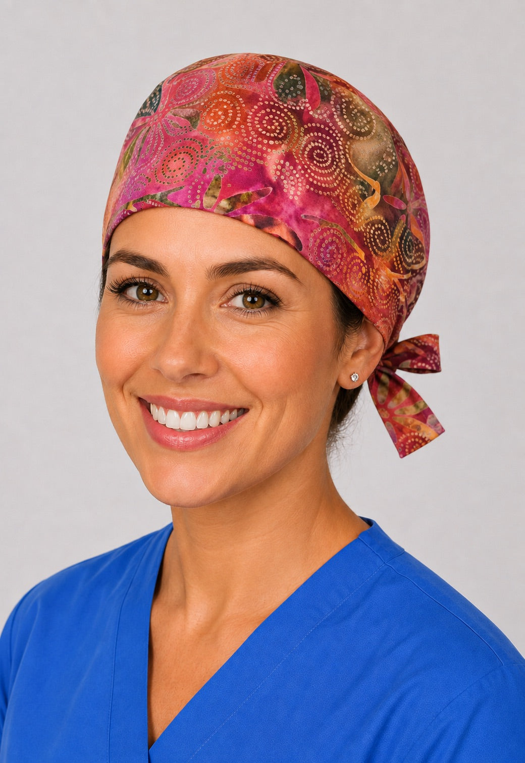 Sunset batik surgical hat with side tie, magenta and coral dot swirl print on a woman in scrubs