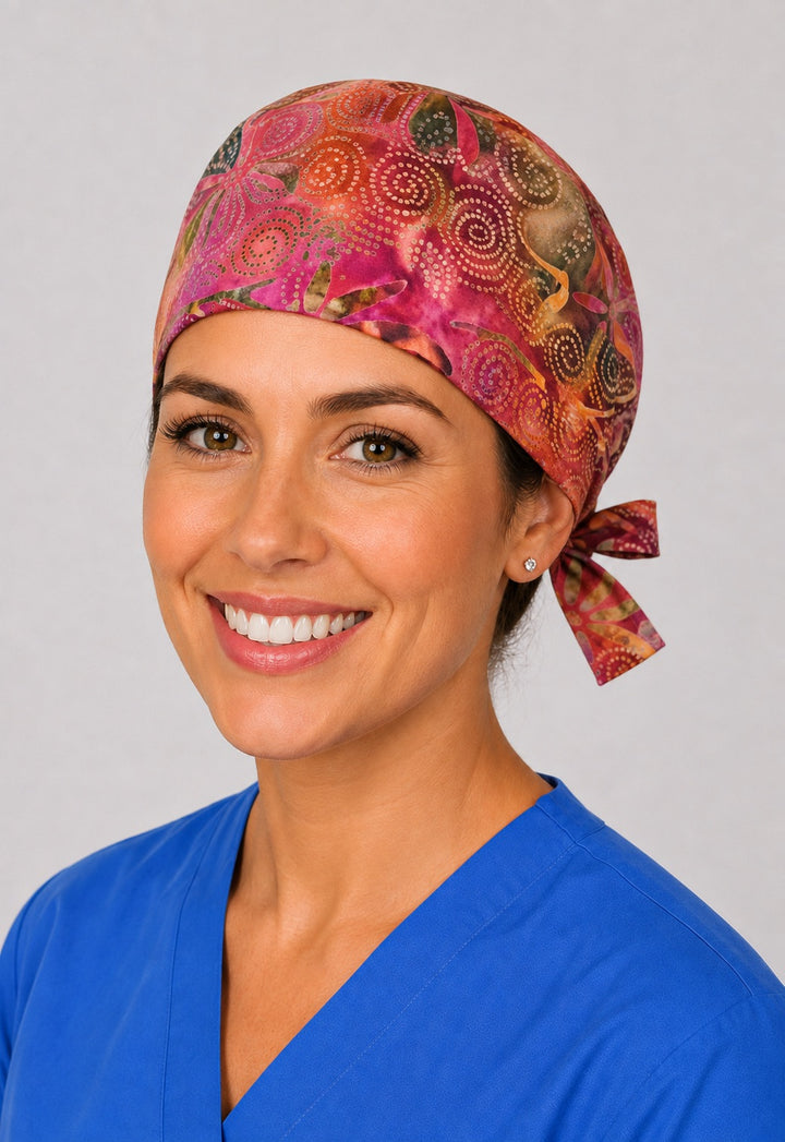 Sunset batik surgical hat with side tie, magenta and coral dot swirl print on a woman in scrubs
