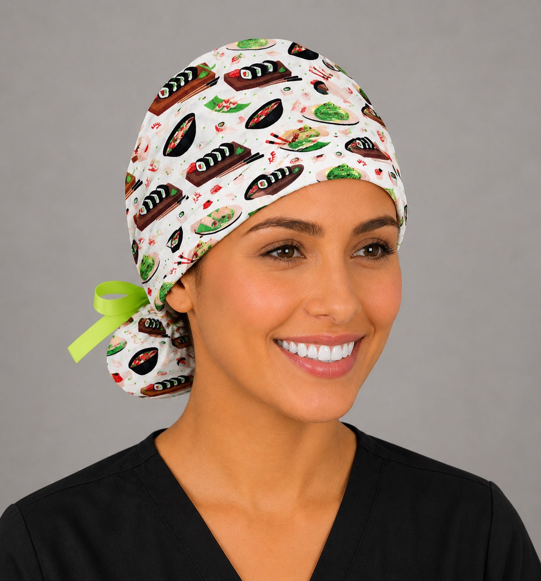 Sushi ponytail scrub cap left front angle on smiling model showing Japanese food print of sushi rolls, ramen and chopsticks with lime green ribbon