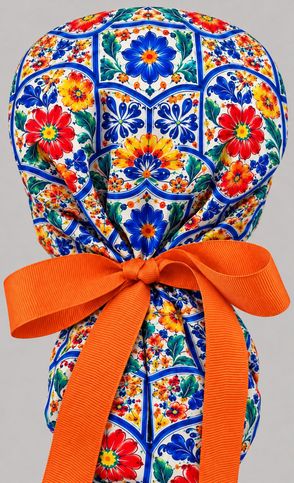 Back view of a Talavera ponytail scrub cap with the gathered tile print pouch and long orange grosgrain ribbon tails tied in a bow