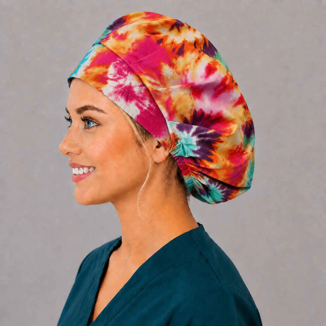 Woman wearing a tie-dye bouffant scrub cap, front view — rainbow hippie spiral sunbursts, adjustable women&