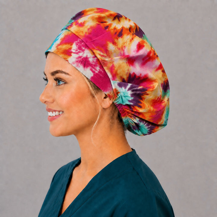 Woman wearing a tie-dye bouffant scrub cap, front view — rainbow hippie spiral sunbursts, adjustable women&