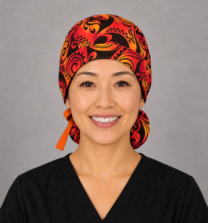 Woman wearing a Tribal Flame ponytail scrub cap, front smiling view — red, orange and black tribal print, orange ribbon tie