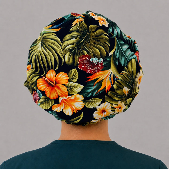 Tropical floral bouffant scrub cap back view showing full print of orange hibiscus, bird of paradise and monstera leaves on black, OR World tropical surgical hat