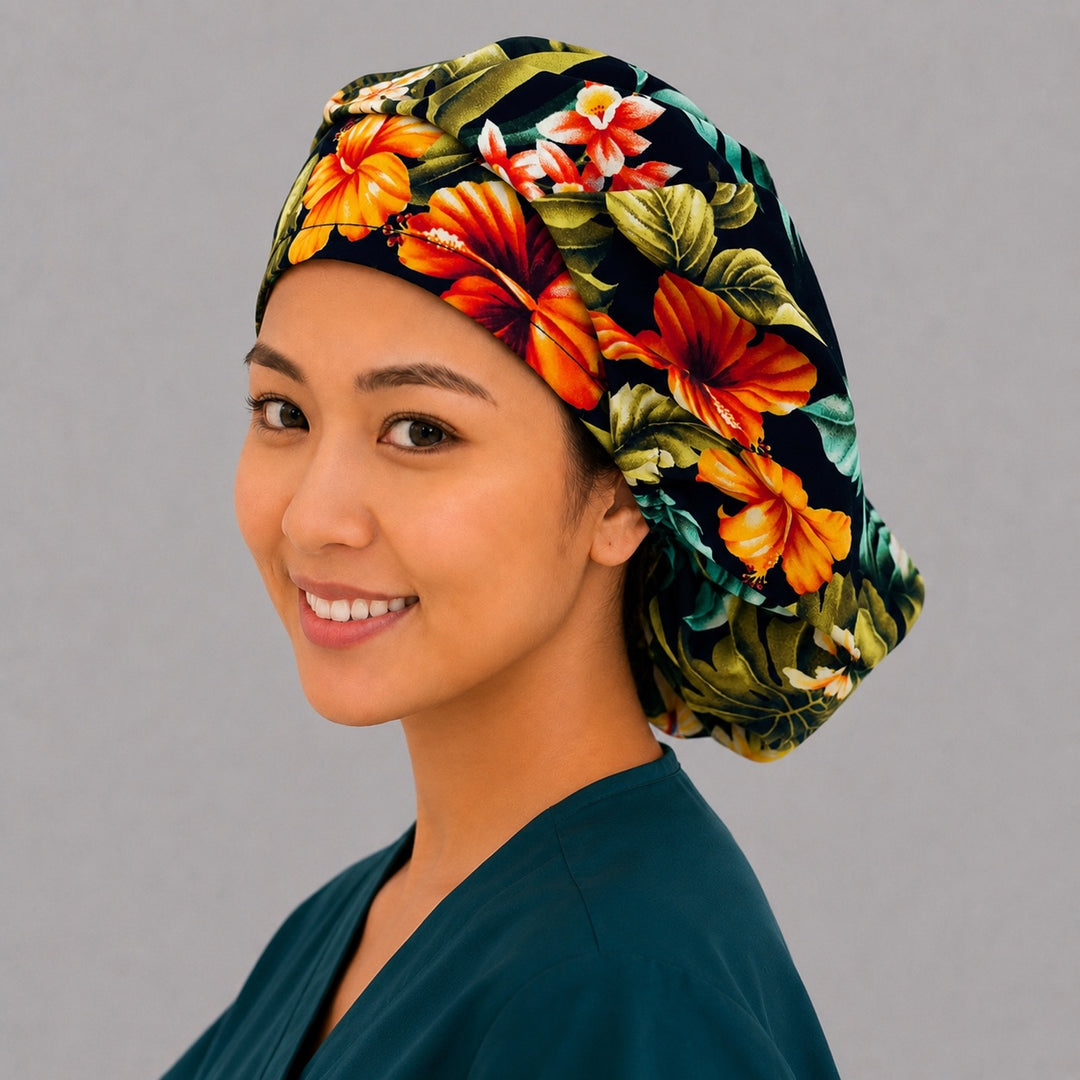 Tropical floral bouffant scrub cap left three-quarter angle on smiling model showing orange and red hibiscus with green leaves on black, women's tropical surgical hat OR World