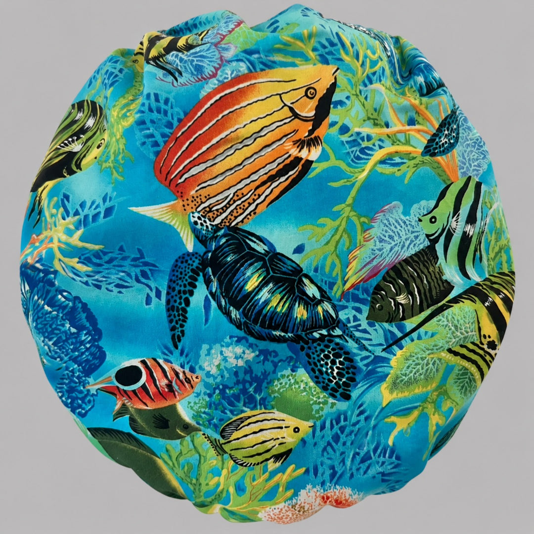 Woman wearing a tropical ocean bouffant scrub cap, front view — sea turtle, coral reef and colorful fish on turquoise with blue band, adjustable women&