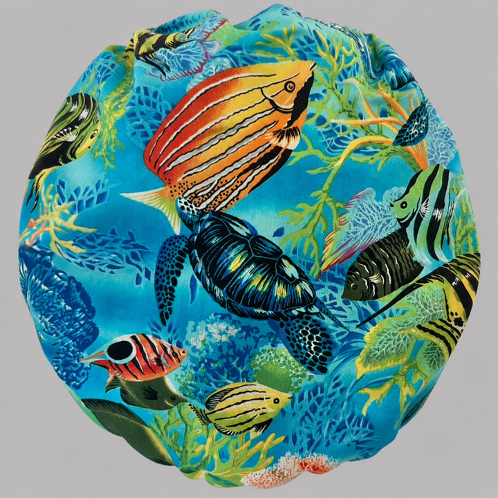 Woman wearing a tropical ocean bouffant scrub cap, front view — sea turtle, coral reef and colorful fish on turquoise with blue band, adjustable women&