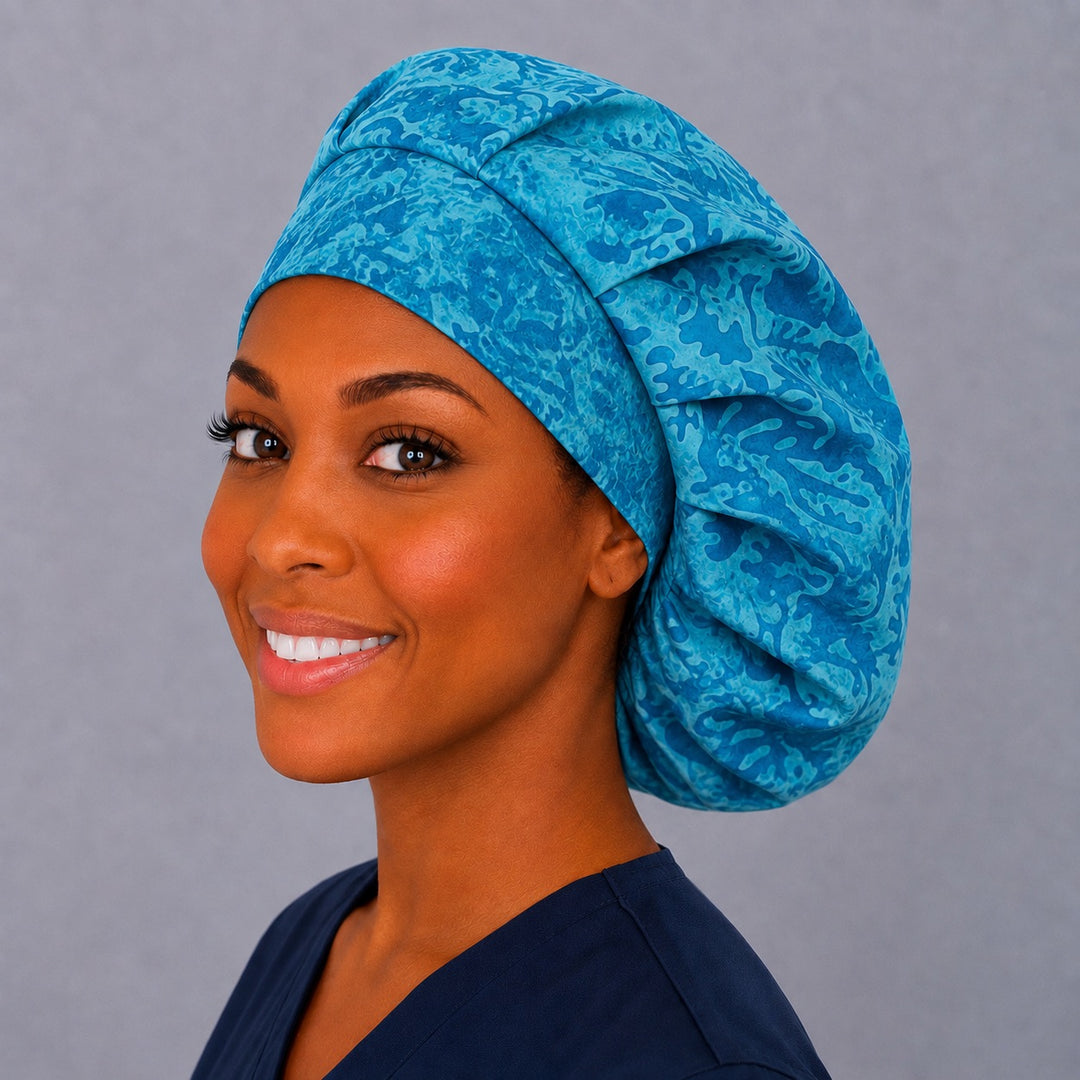 Woman wearing a turquoise batik bouffant scrub cap — blended aqua and teal swirl print, roomy adjustable surgical hat for women