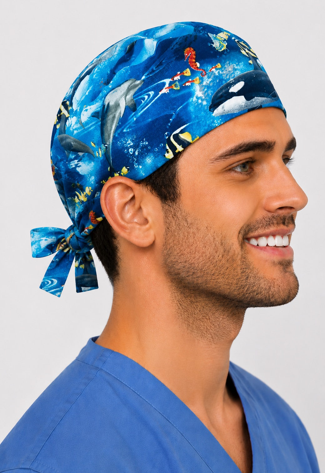 Underwater Paradise ocean scrub cap, front three quarter view on a smiling male nurse in blue scrubs, dolphin orca and tropical fish marine tie back surgical hat, handmade in USA by OR World.