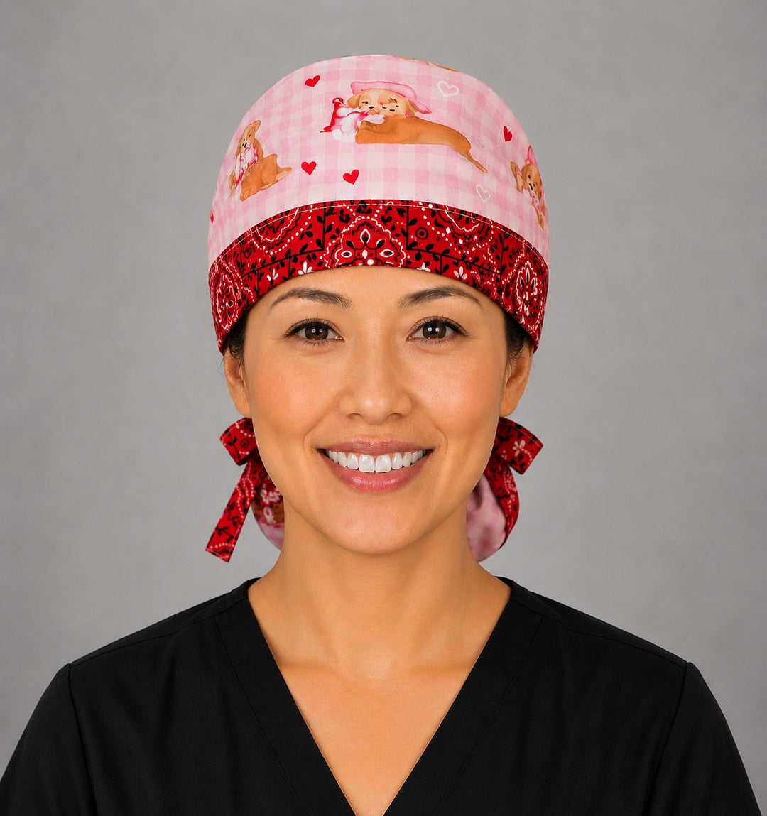 Valentine dogs ponytail nurse cap left three-quarter angle on smiling model showing puppies, hearts and bows on pink gingham with red bandana band and red ribbon bow