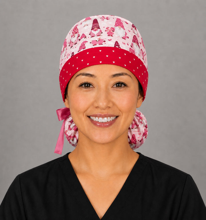 Valentine gnomes ponytail nurse cap left three-quarter angle on smiling model showing red and pink gnomes, hearts and LOVE banner with red heart band and pink ribbon bow