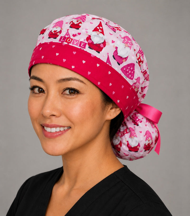 Valentine gnomes ponytail scrub cap right front angle on smiling model showing red and pink gnomes and XO hearts on pink with red heart band and pink ribbon