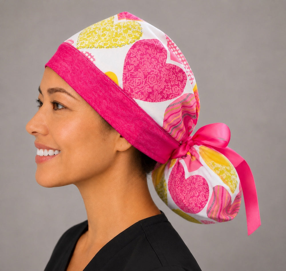 Valentine's hearts ponytail nurse cap left three-quarter angle on smiling model showing pink, yellow and lime hearts on white with hot pink ribbon bow
