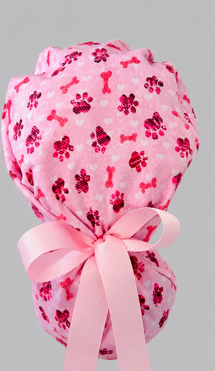 Valentine puppy paws and bones ponytail scrub cap left side profile with full ponytail pouch of pink and red paw prints, dog bones and long pink ribbon ties