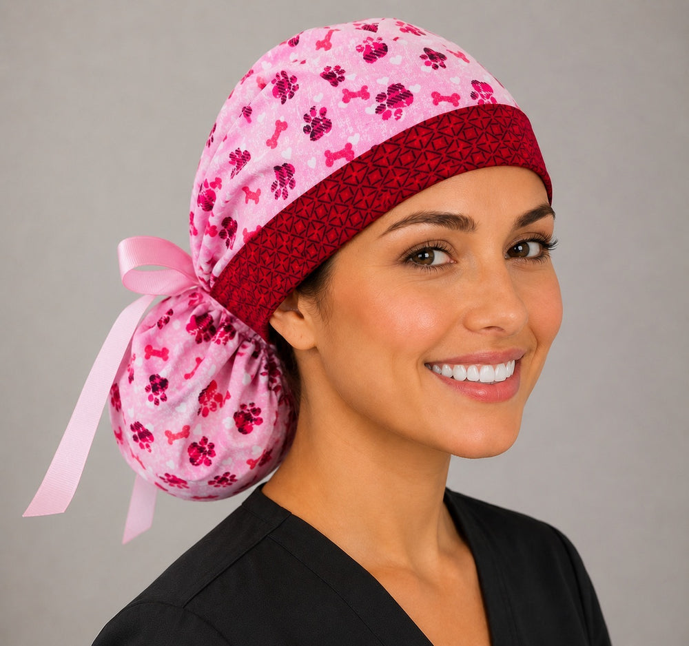 Valentine puppy paws and bones ponytail nurse cap left three-quarter angle on smiling model showing pink and red paw prints, dog bones and pink ribbon bow
