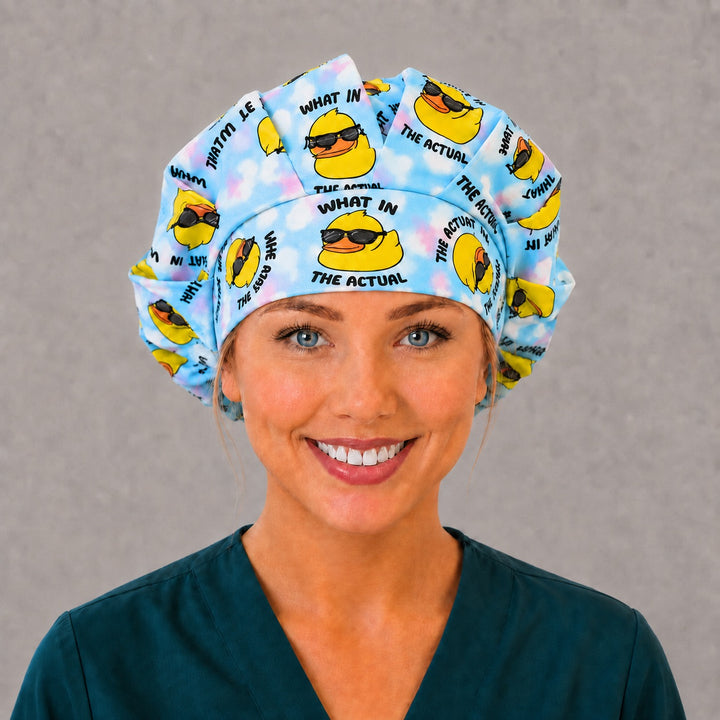 Woman wearing a What in the Actual Duck bouffant scrub cap, front view — rubber ducks in sunglasses on blue tie-dye, adjustable women&