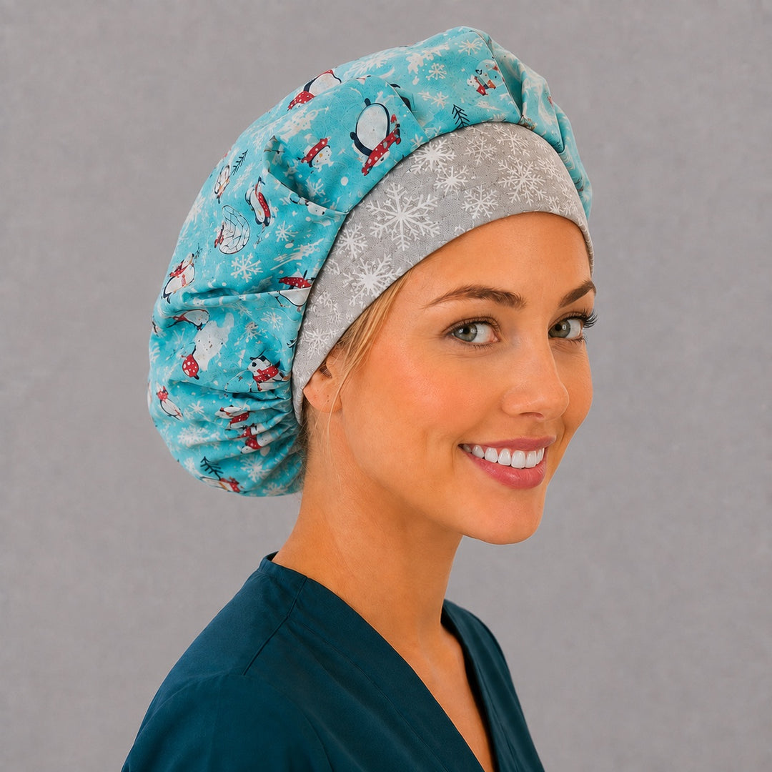 Woman wearing a winter penguin bouffant scrub cap, front view — aqua penguin print with grey snowflake band, adjustable women&