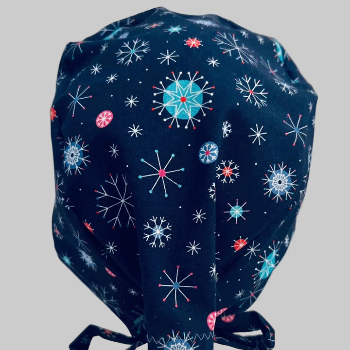 Traditional navy scrub cap with colorful blue, white, and red snowflake print, adjustable tie-back surgical cap for nurses, surgeons, doctors, healthcare professionals, Christmas holiday medical scrub hat, back view