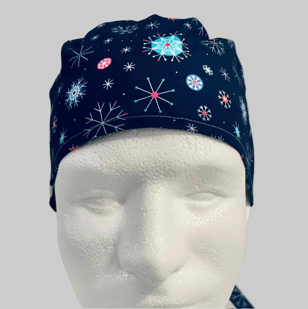 Traditional navy scrub cap with colorful blue, white, and red snowflake print, adjustable tie-back surgical cap for nurses, surgeons, doctors, healthcare professionals, Christmas holiday medical scrub hat, front view