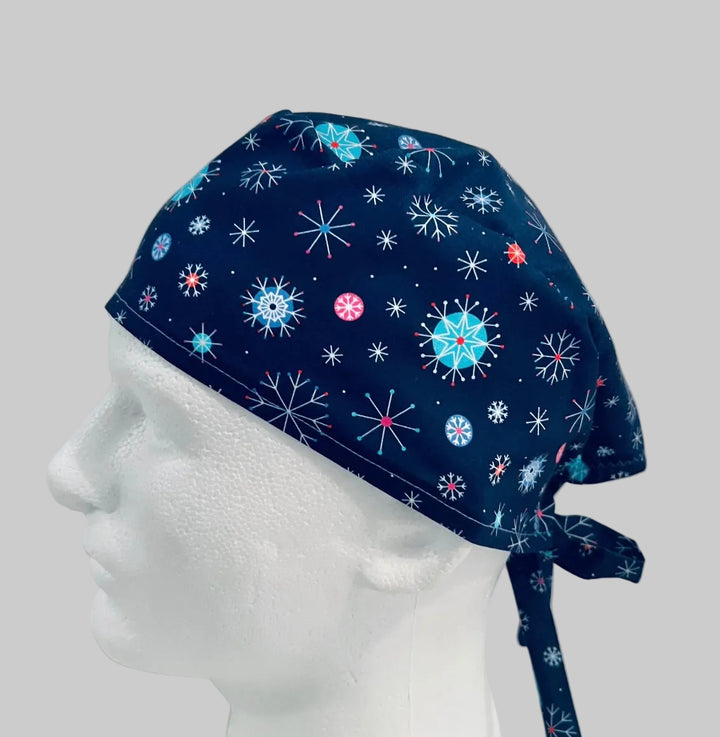 Traditional navy scrub cap with colorful blue, white, and red snowflake print, adjustable tie-back surgical cap for nurses, surgeons, doctors, healthcare professionals, Christmas holiday medical scrub hat, left side view