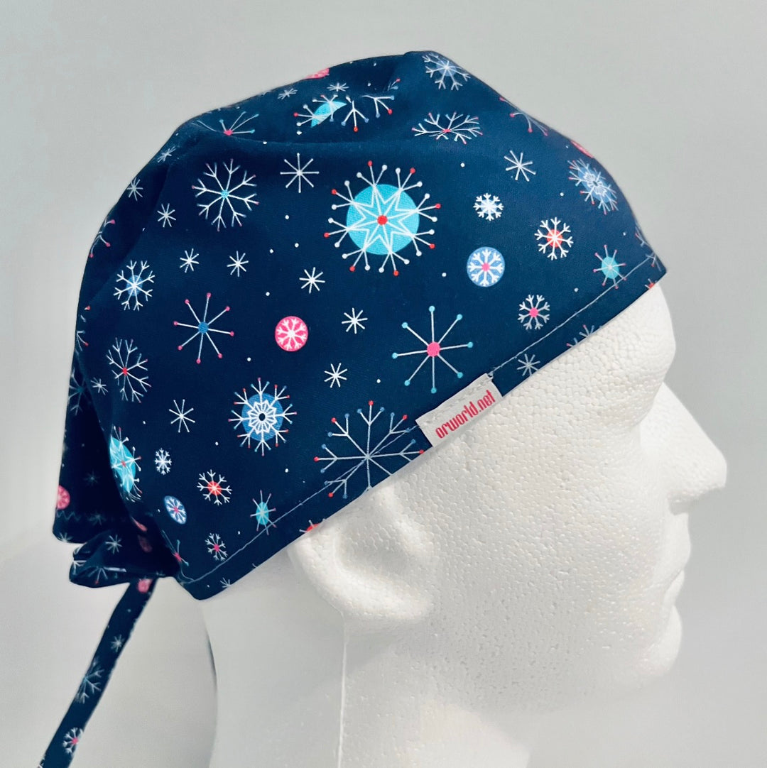 Traditional navy scrub cap with colorful blue, white, and red snowflake print, adjustable tie-back surgical cap for nurses, surgeons, doctors, healthcare professionals, Christmas holiday medical scrub hat, right side view.