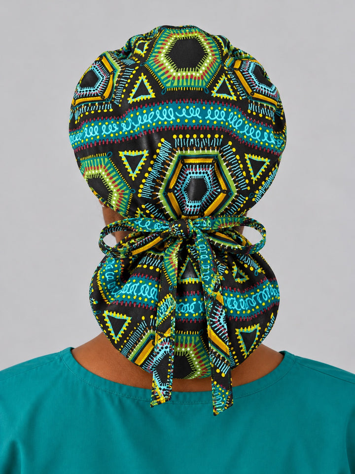 Back view of an XL Ankara ponytail nurse hat, showing full rear coverage, a hexagon medallion on the crown and long fabric ties hanging over the pouch
